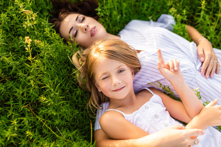 happy mother and daughter relaxing while lying in flowery meadowの写真素材