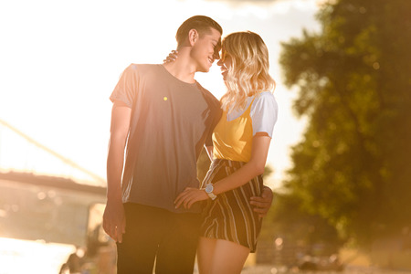 young couple hugging and going to kiss on river beach during sunsetの写真素材