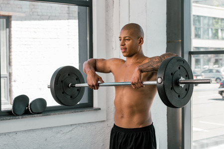 handsome young african american sportsman lifting barbell in gym