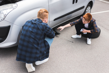 father lifting car with floor jack for changing tire, son pointing on somethingの写真素材