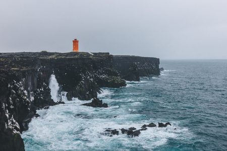 scenic shot of red lighthouse on rocky cliff in Iceland on stormy dayの写真素材