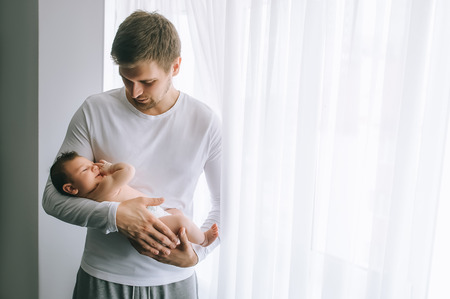 father carrying little baby boy in front of curtains at homeの写真素材