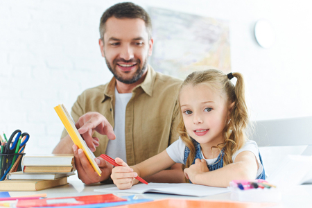 smiling father and little daughter doing homework together at homeの写真素材