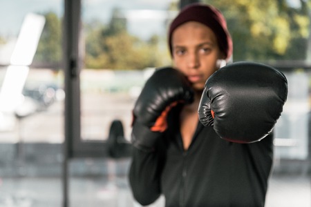 selective focus of african american male boxer in boxing gloves exercising at gymの写真素材