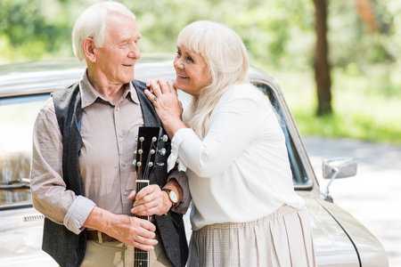 senior husband and wife looking at each other and man holding guitar leaning on carの写真素材