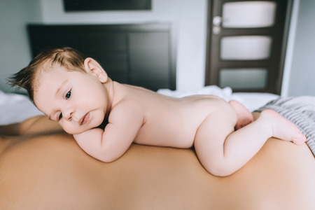 selective focus of infant boy laying on father back in bed at homeの写真素材