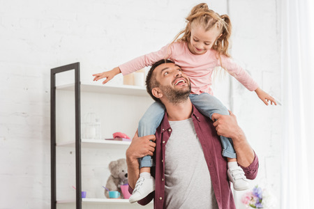 daughter sitting on fathers back and having fun at homeの写真素材