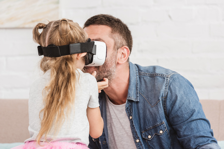 father and smiling daughter using virtual reality headset together at homeの写真素材