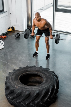 high angle view of athletic bare-chested african american sportsman lifting barbell in gym