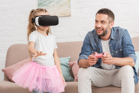 happy father and daughter playing with joystick and virtual reality headset at homeの写真素材