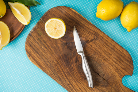 top view of lemons and knife on wooden cutting board on turquoise backgroundの写真素材