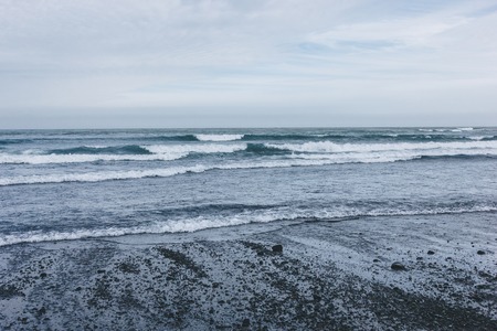 ocean waves covering black sandy beach in Icelandの写真素材
