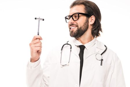 smiling doctor in white coat and eyeglasses holding reflex hammer isolated on whiteの写真素材