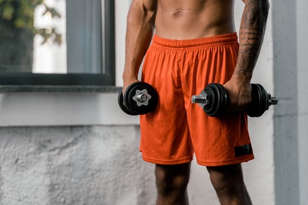 cropped image of tattooed african american sportsman exercising with dumbbells at gymの写真素材