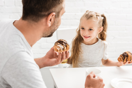 father and daughter having croissants for breakfast and looking at each otherの写真素材