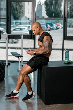 side view of muscular young tattooed african american sportsman using digital tablet in gymの写真素材