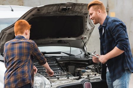 ginger hair father and son repairing car with open hoodの写真素材