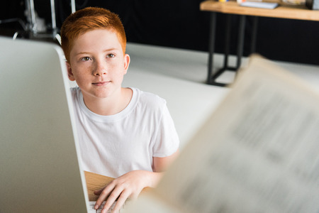 boy sitting at table with computer and looking away at home