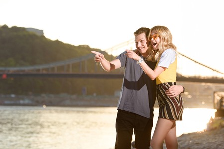 young couple pointing on something at river beach during sunset