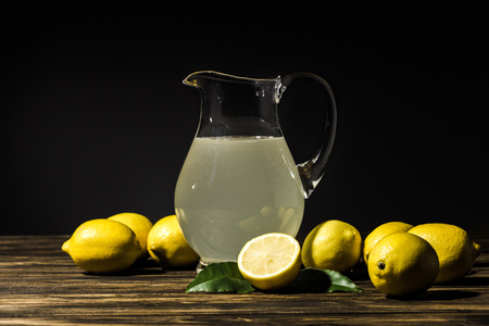 glass jug with organic juice and yellow lemons around on wooden tabletopの写真素材