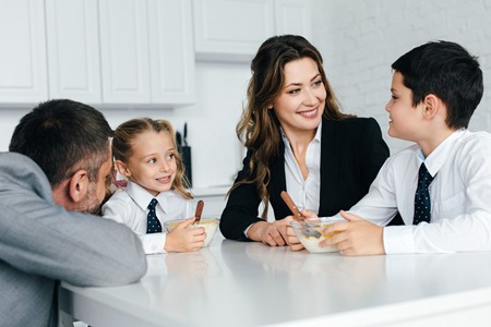 family in suits and school uniform having breakfast in kitchen togetherの写真素材