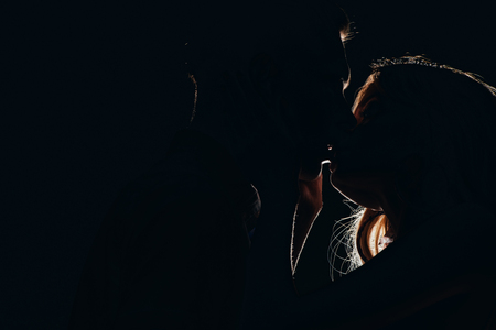 silhouettes of passionate heterosexual couple kissing in darkの写真素材