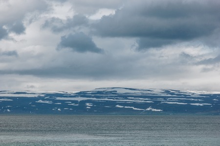 dramatic shot of lake under cloudy sky in Iceland with snowy mountains on backgroundの写真素材
