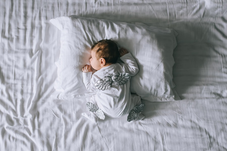 overhead view of little baby boy in costume with wings laying in bed at home