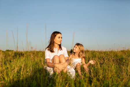 mother and daughter sitting on green grass on sunset and chattingの写真素材