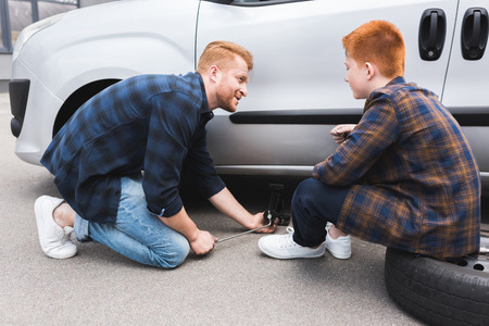 father lifting car with floor jack for changing tire, son looking at himの写真素材