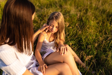 mother and daughter sitting together on grass in eveningの写真素材