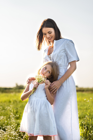 beautiful mother and daughter with field flowers bouquet embracing in green meadowの写真素材