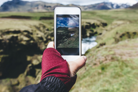 cropped image of woman taking picture of landscape with Skoga river on smartphone in Icelandの写真素材