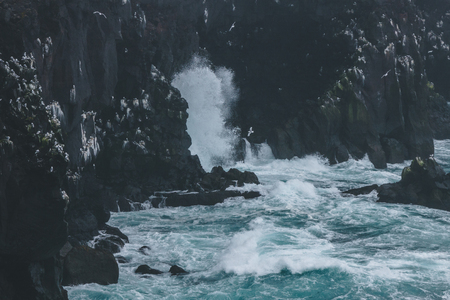 dramatic shot of ocean waves crashing on rocky cliffs in Icelandの写真素材