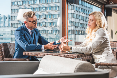 Businesswoman and businessman talking in cafe and holding smartphone with glassesの写真素材