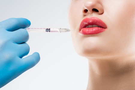 Cropped view of doctor making beauty injection in lips for woman, isolated on whiteの写真素材