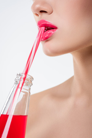 Close up view of girl drinking pink beverage from bottle with straw, isolated on whiteの写真素材