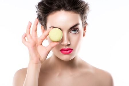 Young stylish woman holding green macaroon in front of eye, isolated on whiteの写真素材