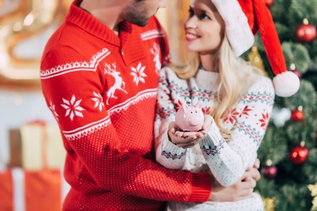 Couple in santa hats holding piggy bank with banknote at home on christmas eveの写真素材