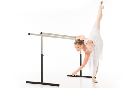 Ballerina in tutu and pointer shoes practicing at ballet barre stand isolated on white backgroundの写真素材