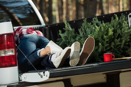 Partial view of young couple laying in car trunk with Christmas tree and cup outdoors