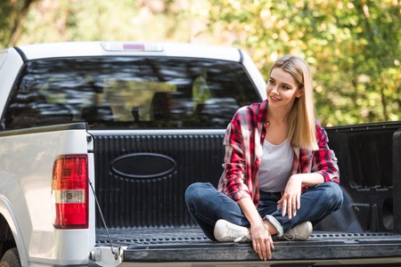 Selective focus of young woman sitting in trunk of pick up car outdoors