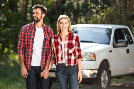 Happy young couple holding hands near pick up car in forest