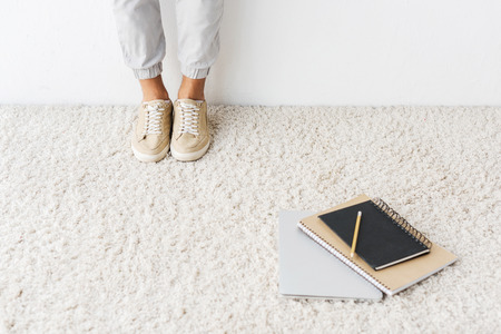 cropped view of casual man standing on beige rug with laptop and notebooksの写真素材