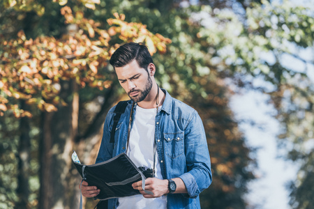 portrait of young focused traveler with map standing in autumn park