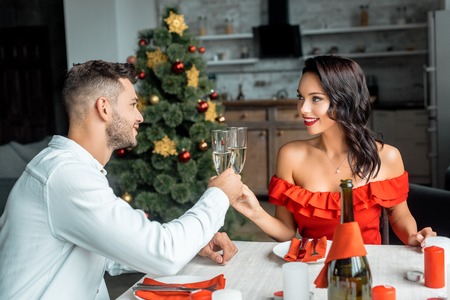 cheerful couple celebrating christmas and clinking by champagne glasses at served table with candles at homeの写真素材