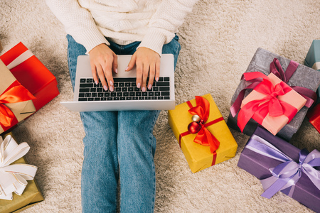 cropped shot of young woman using laptop while sitting near christmas giftsの写真素材