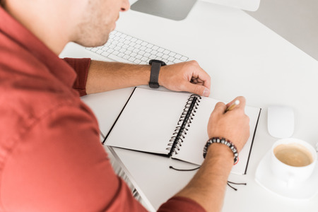 cropped view of businessman writing in notebook in modern office
