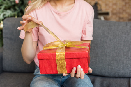 cropped shot of young woman sitting on sofa and opening christmas presentの写真素材