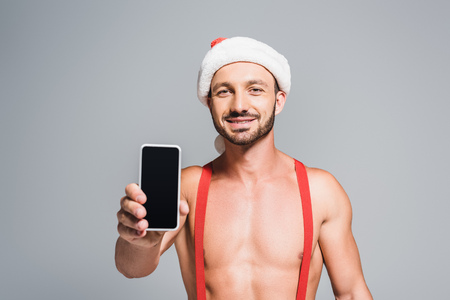 happy muscular man in christmas hat showing smartphone with blank screen isolated on grey backgroundの写真素材
